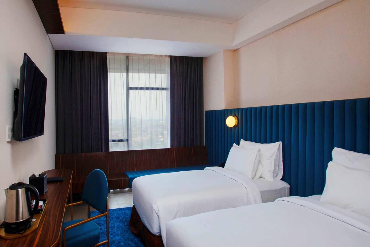 A hotel room with two beds, a desk with a chair, a TV, and a window with curtains.