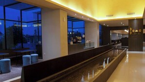 Un moderno vestíbulo de hotel con una larga fuente rectangular, grandes ventanales y un área de estar con otomanas azules.