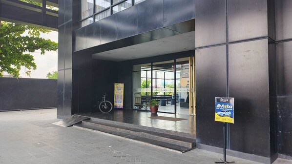 A modern building entrance with a ramp leading to a covered area, a bicycle, and a car rental sign. - Bono Hotel by ARTOTEL - Pekanbaru (Pekanbaru)