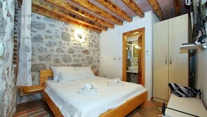 A bedroom with a stone wall, wooden ceiling beams, a bed with white linens, and a wooden wardrobe. - Wonderful home with swimming pool and sauna. Sea view (Starigrad)
