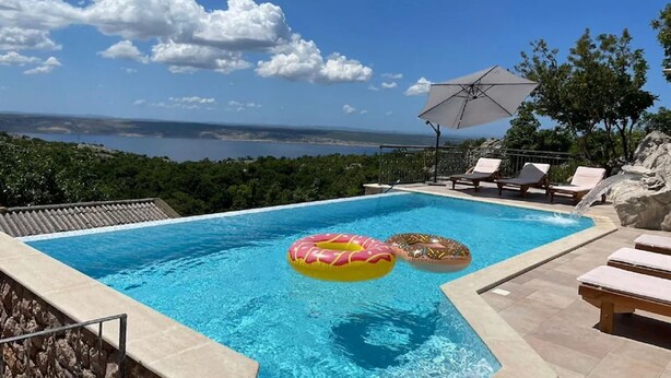 A swimming pool with clear blue water, surrounded by lounge chairs and a large umbrella. - Wonderful home with swimming pool and sauna. Sea view (Starigrad)