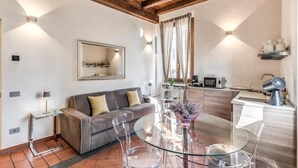 Un salon moderne avec une table en verre, un canapé gris et un coin cuisine équipé d’un four à micro-ondes et d’une bouilloire.