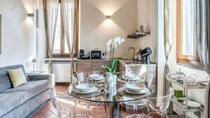 Un salon moderne avec une table à manger en verre pour quatre personnes, un canapé et une cuisine en arrière-plan.