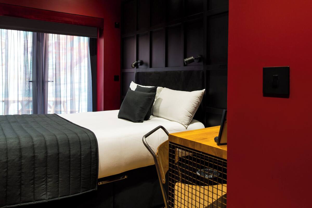 A hotel room with a bed, a desk, a chair, and a window with curtains.