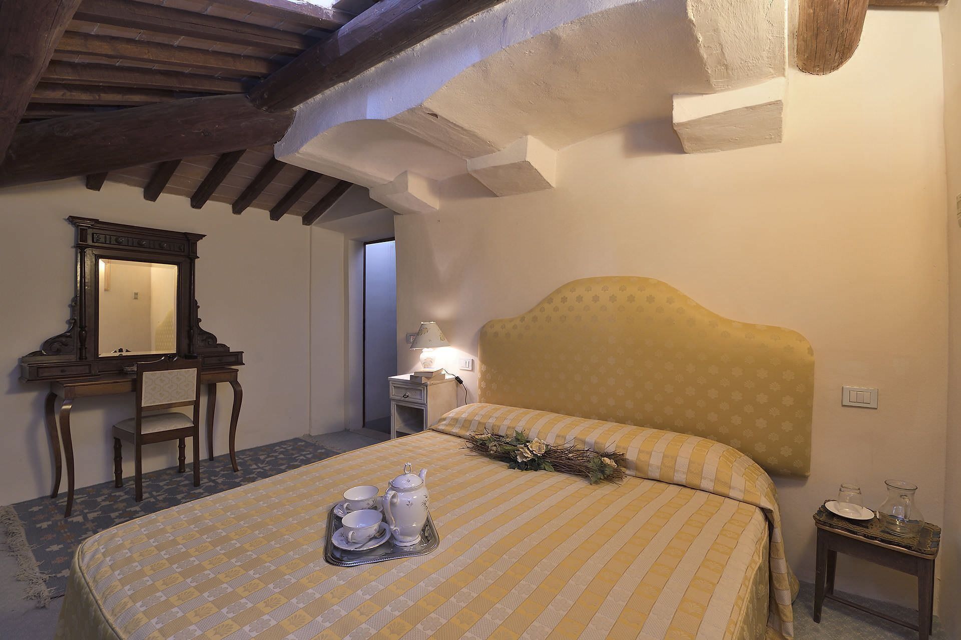 Um quarto com uma cama, uma mesa de cabeceira, um espelho e uma escrivaninha.