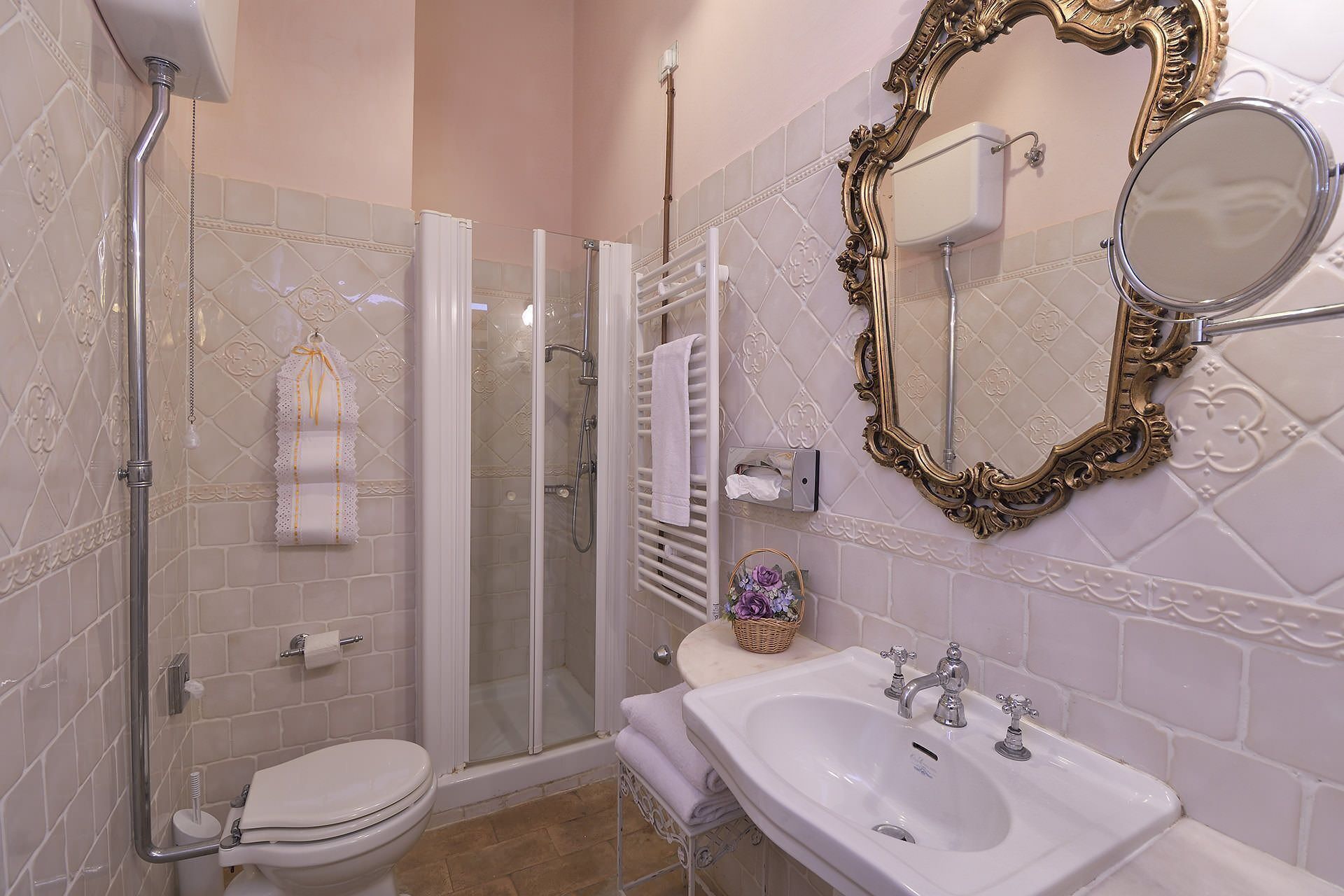 A bathroom with a glass-enclosed shower, a white toilet, a sink with two faucets, and a decorative mirror with an ornate frame.