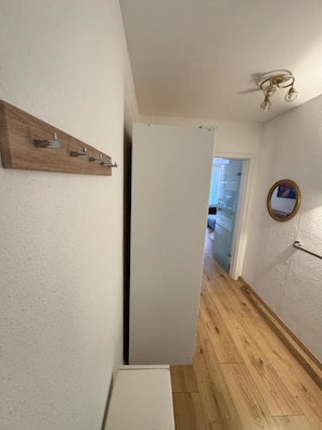A hallway with a wooden shelf, a white door, a mirror, and a light fixture.