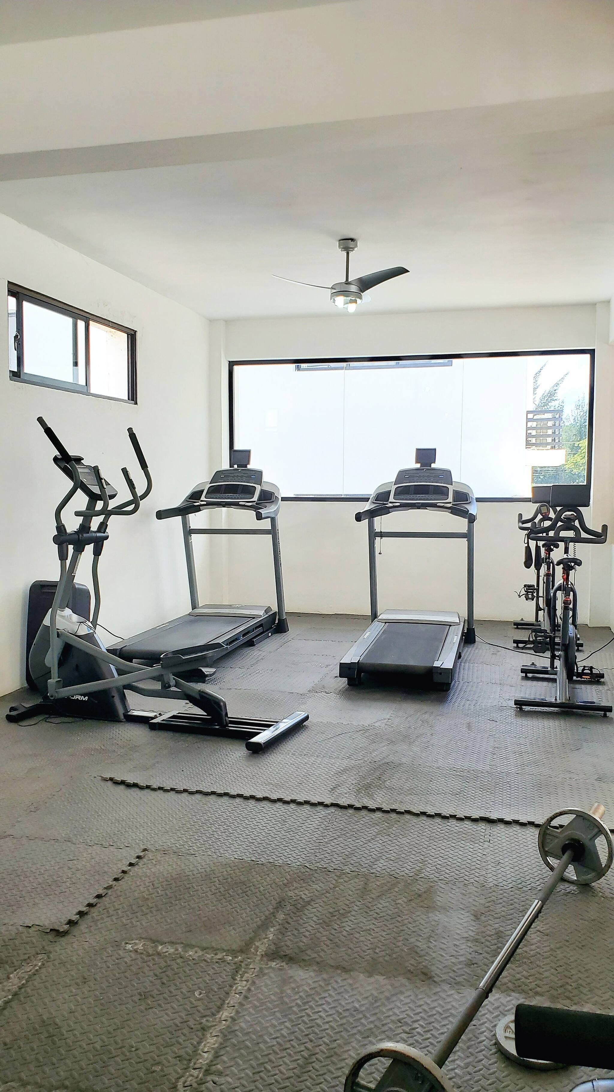 A gym with treadmills, stationary bikes, and a ceiling fan.