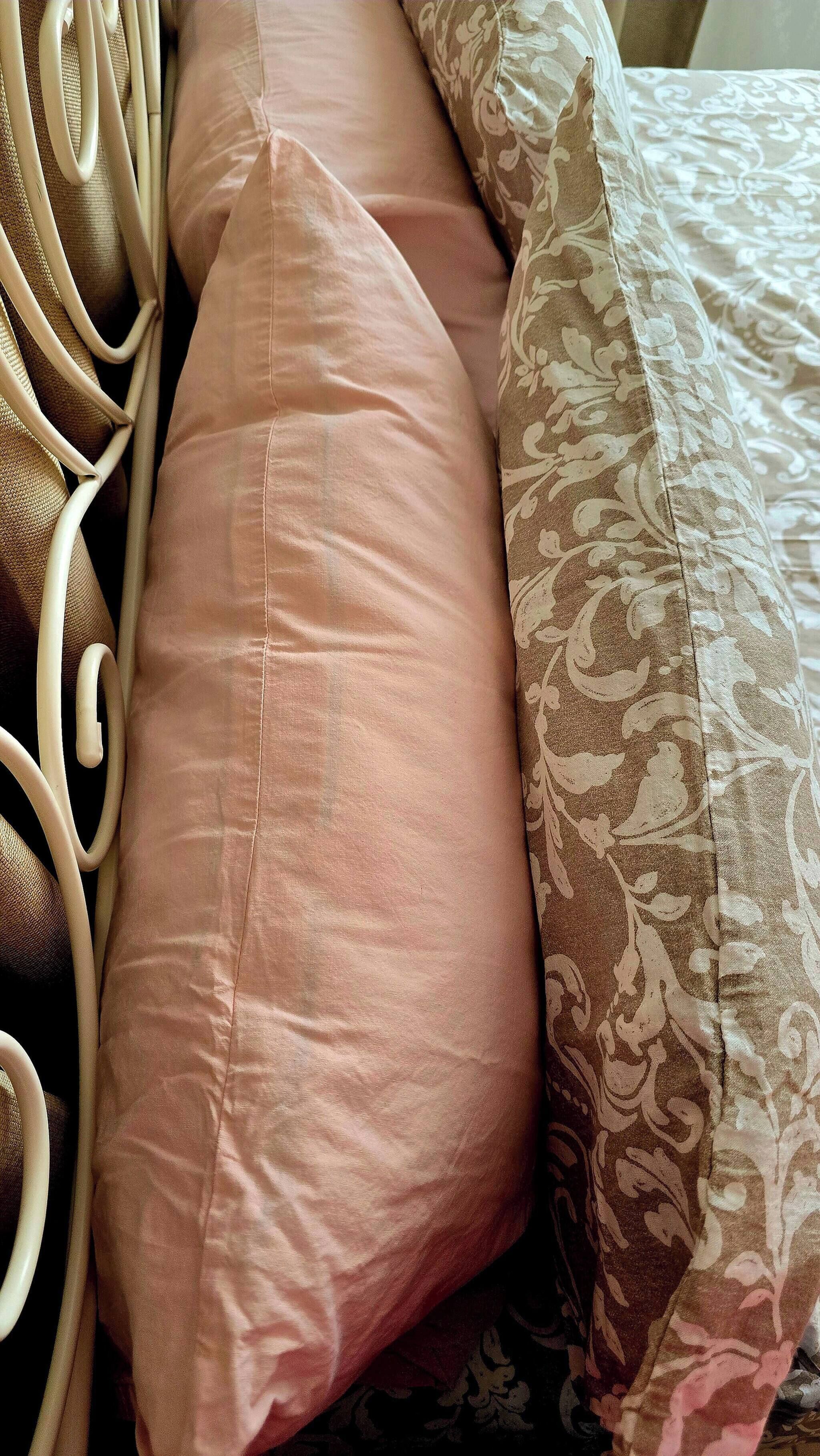 A bed with a patterned blanket and two pillows, one pink and one beige.