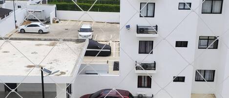 A multi-story building with a white exterior, multiple balconies, and a parking area with several cars.