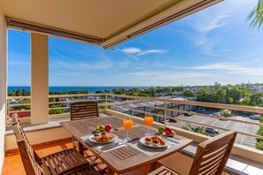 Un balcon avec une table préparée pour le petit-déjeuner, offrant une vue sur le paysage urbain et la mer.