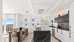 Een moderne keuken met een marmeren eiland, witte kasten en een eethoek met houten stoelen en een tafel.