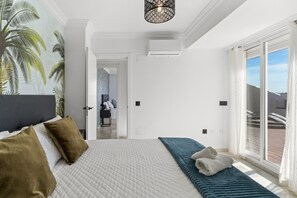 A bedroom with a bed, a bedside table, a chair, a window with a view, and a ceiling light fixture. - Apartment 'Marbella Ático las Vistas De Laia' with Sea View, Wi-Fi and Air Conditioning (Marbella)