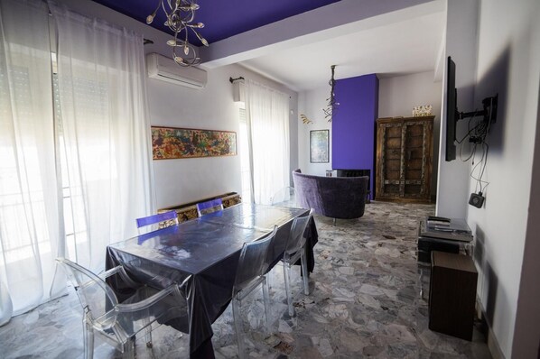 A dining area with a long table, clear chairs, and a purple accent wall. - Elegante appartamento in centro città (Reggio Calabria)