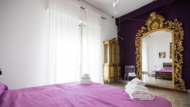 Una habitación de hotel con una cama morada, un espejo dorado ornamentado y un armario grande.