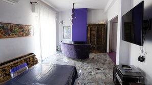 Una habitación con una cama, una silla morada, un televisor y un suelo de piedra.