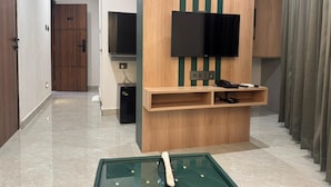 Una sala de estar moderna con un televisor de pantalla plana montado en una pared de madera con detalles verde, una mesita con cubierta de vidrio y un sofá.