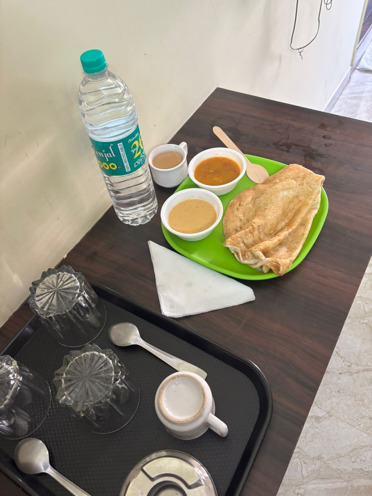Una bandeja con una botella de agua, dos tazas de café, un plato con una crepe doblada y una servilleta.