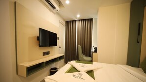 Habitación de hotel con cama, televisor montado en la pared, una silla y un escritorio con lámpara.