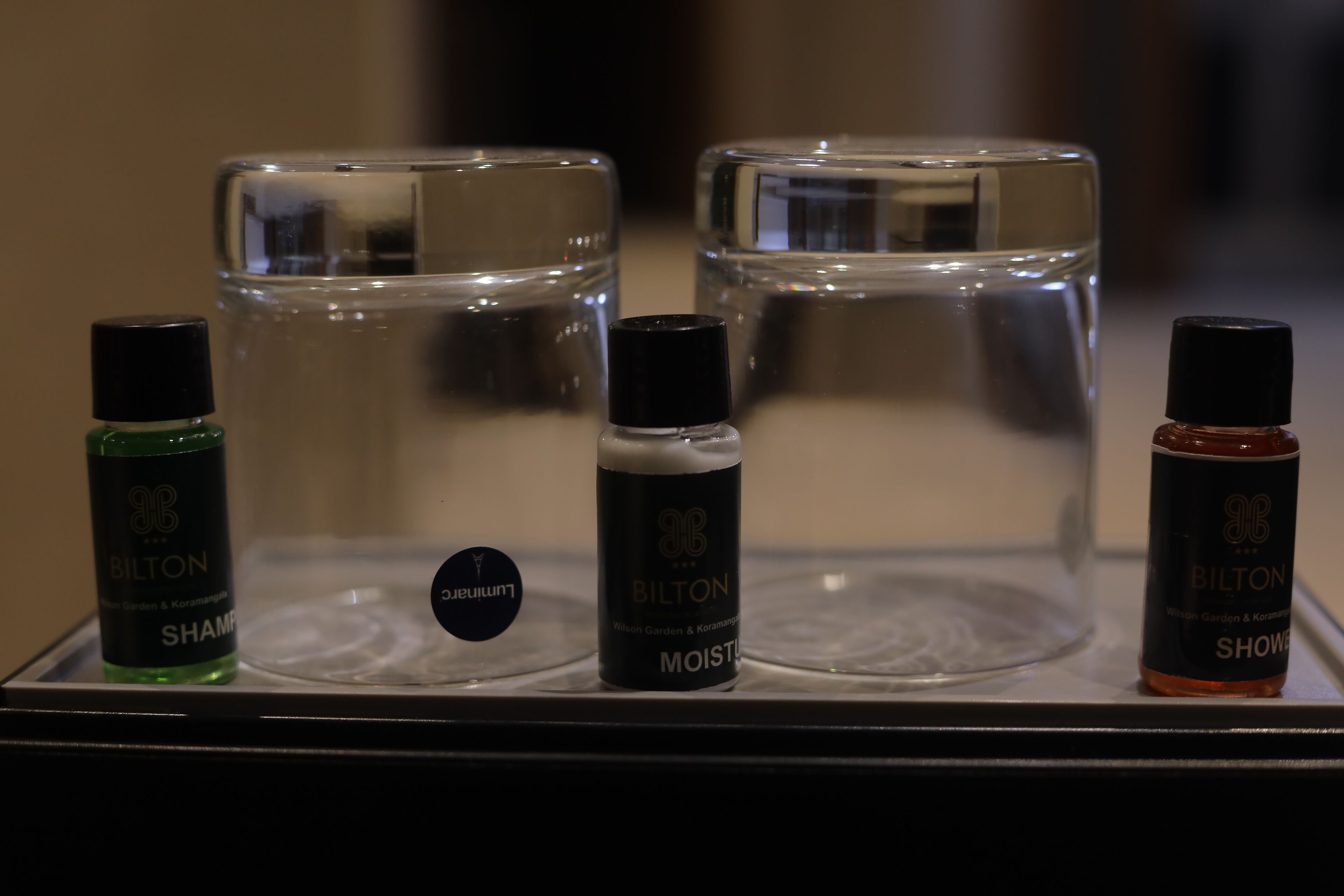 Exposició de tres ampolles de productes BILTON: XAMPÚ, HIDRATA i GEL DE DITZA, disposades sobre un safata.