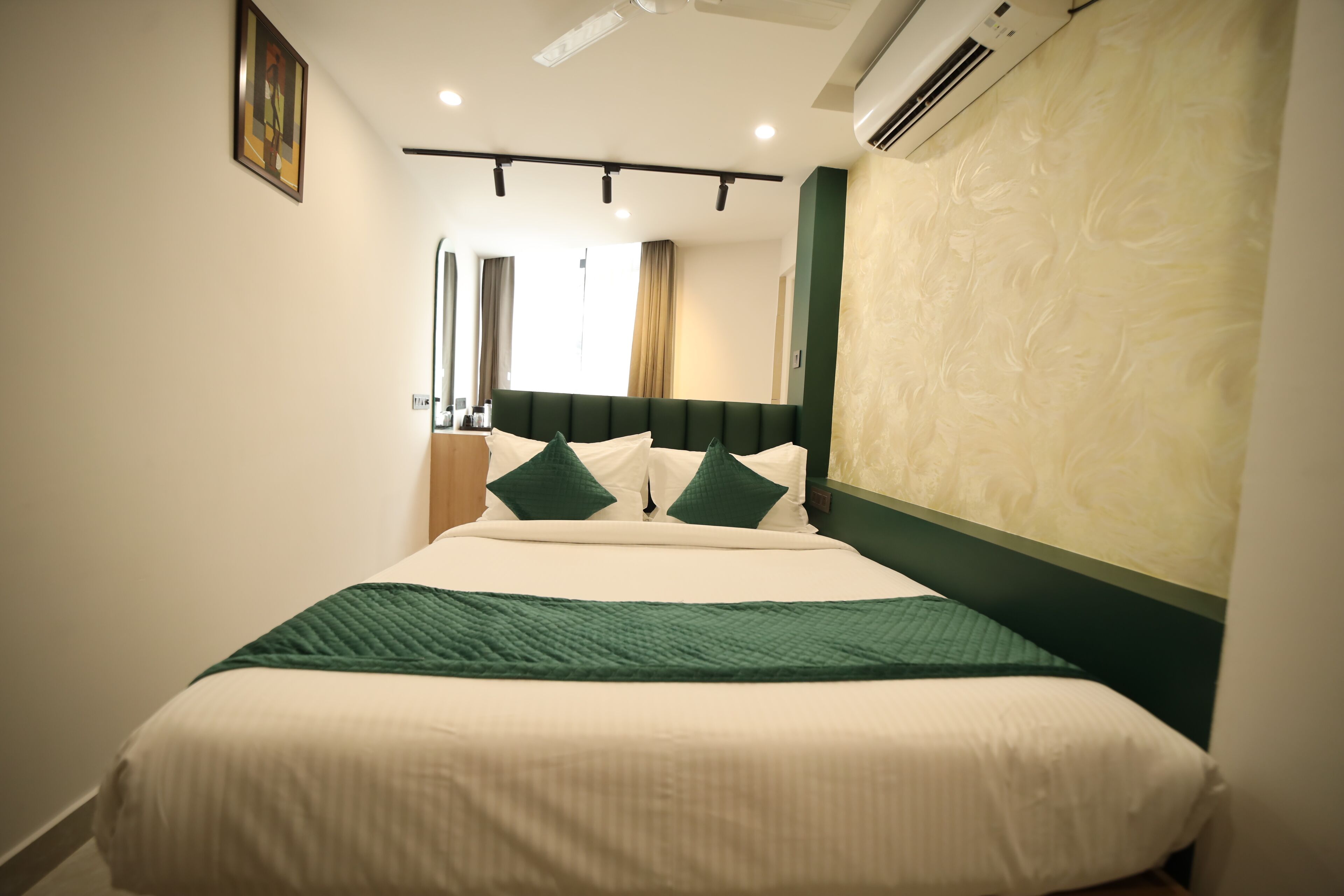 A neatly made bed with a green and white bedspread, a headboard with a green panel, and a wall-mounted air conditioner.