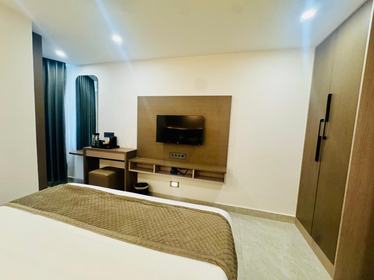 A hotel room with a bed, a desk with a flat-screen TV, a minibar, and a wardrobe.