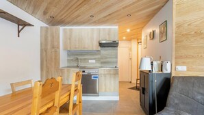 A compact kitchen with wooden cabinets, a dishwasher, and a built-in oven. There is a dining table with chairs and a sofa in the living area.