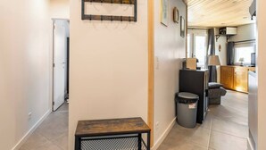 A hallway with a bench, a trash bin, and a wall-mounted rack.
