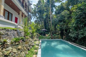 A pool surrounded by lush greenery and a building with a balcony. - Villa Santru  (Ubud)