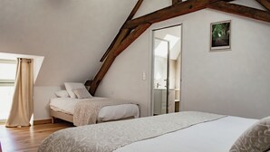 Un dormitorio con techo inclinado, una cama grande, una cama más pequeña y un baño visible a través de una puerta abierta.