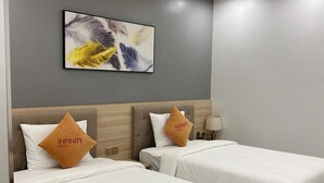 Une chambre d’hôtel avec deux lits, chacun doté de draps blancs et d’une tête de lit en bois. Un tableau abstrait encadré est accroché au mur, au-dessus des lits.