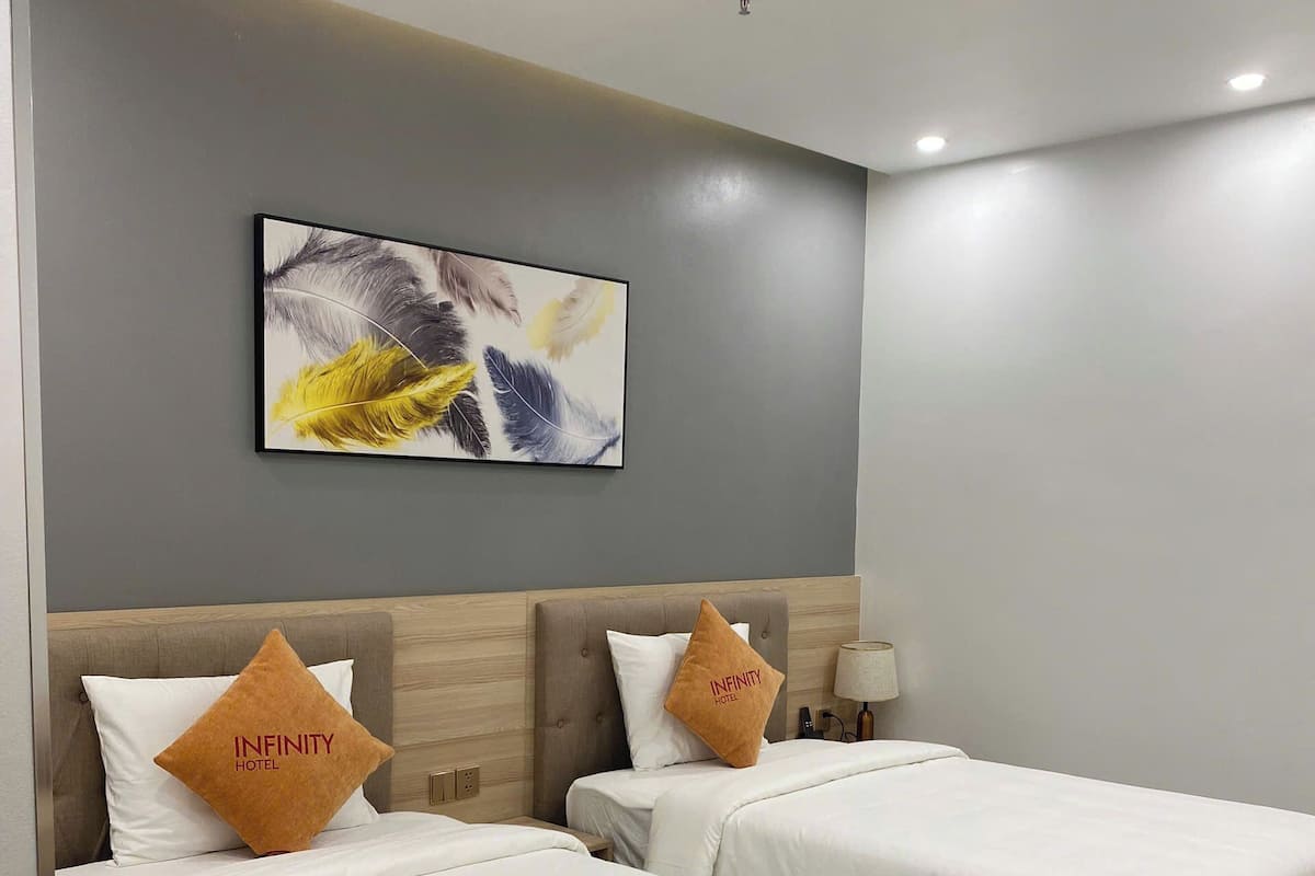 A hotel room with two beds, each with white bedding and a wooden headboard. There is a framed abstract painting on the wall above the beds.