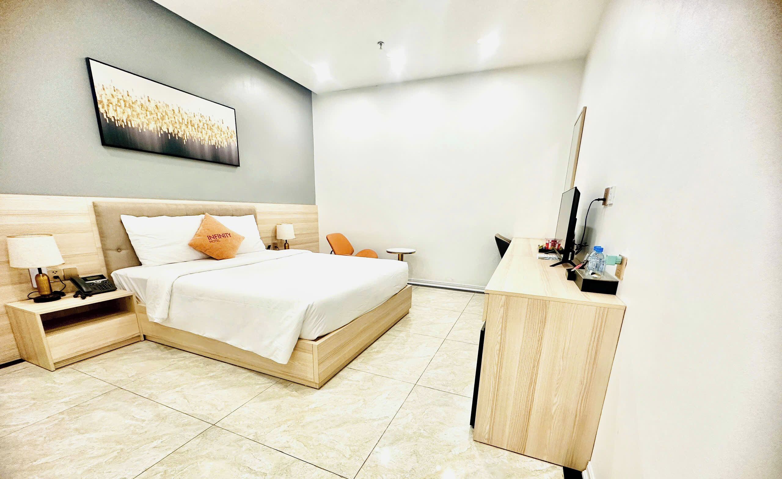Quarto de hotel com cama, mesas de cabeceira, escrivaninha, cadeira e televisão.