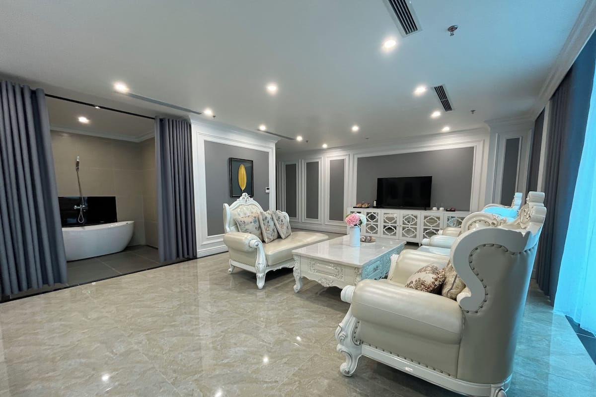 A spacious living room with a large white bathtub, elegant white sofas, a marble floor, and a flat-screen TV on a white cabinet.