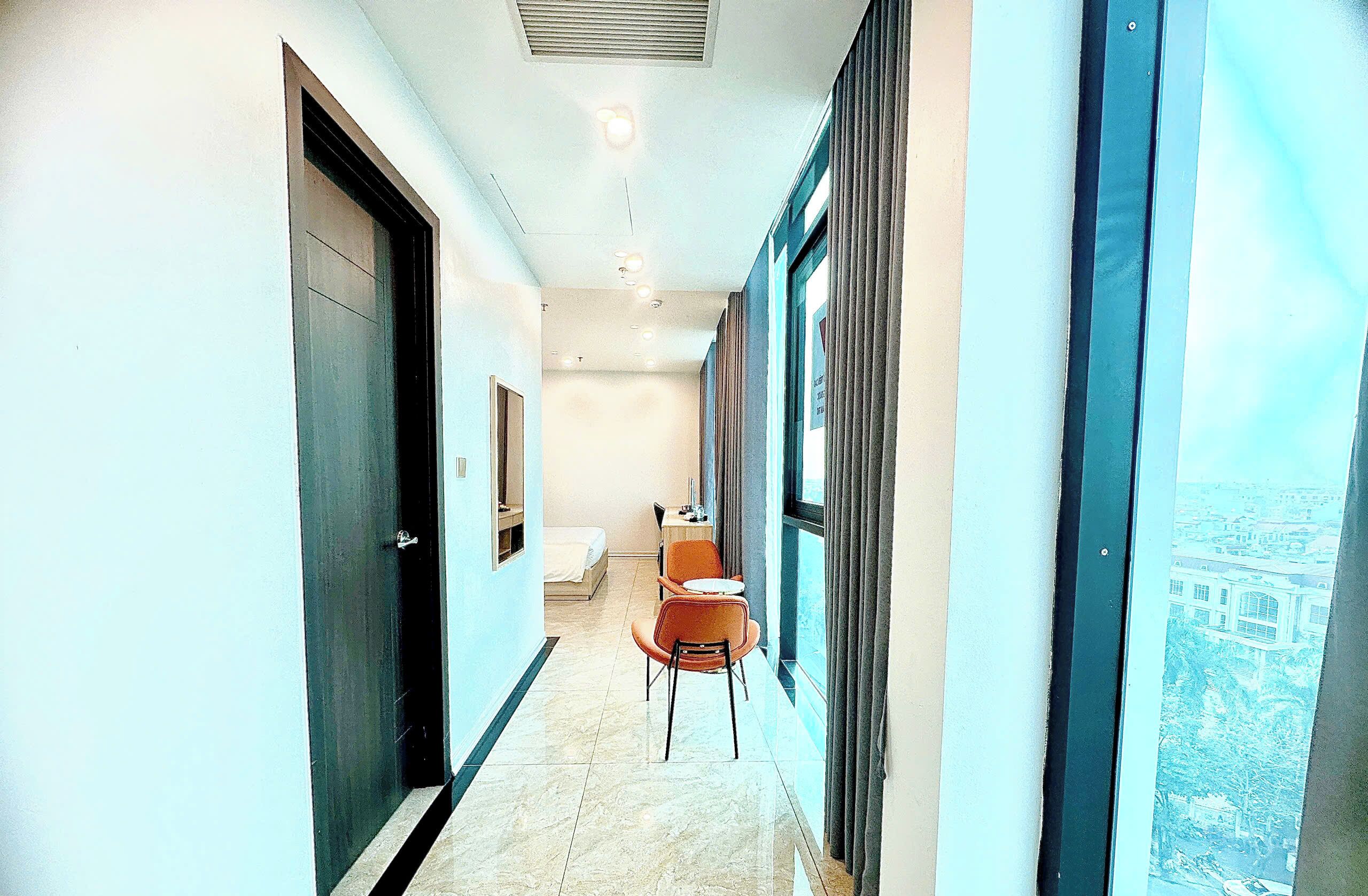 A corridor with a bed, a chair, and a window with a view of buildings.