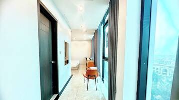 A corridor with a bed, a chair, and a window with a view of buildings.