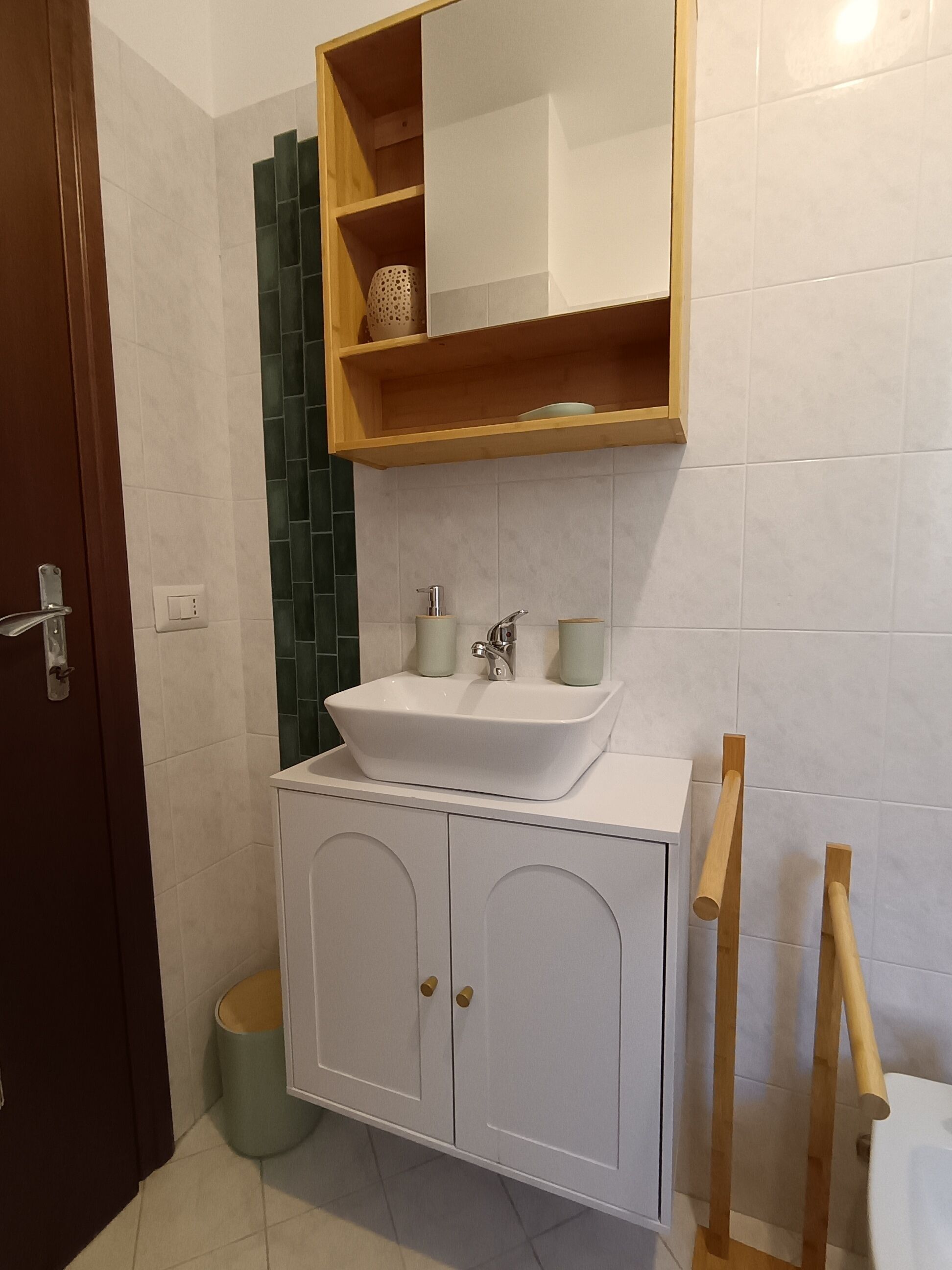 A bathroom with a white sink, wooden shelves, and a green accent wall.