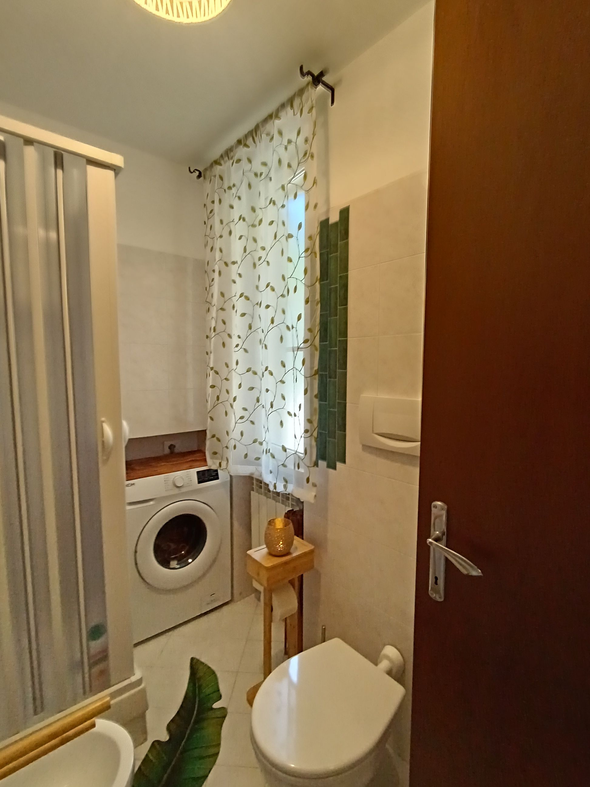 Ein kleines Badezimmer mit Waschmaschine, Toilette und einer kleinen Holzwandablage mit einem Dekoelement.
