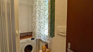 Ein kleines Badezimmer mit Waschmaschine, Toilette und einer kleinen Holzwandablage mit einem Dekoelement.