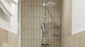 Un petit espace de douche carrelé, équipé d’un pommeau de douche à main et d’un robinet fixé au mur.