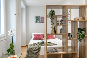 Una camera da letto con un letto, una libreria in legno, un tavolino con una pianta e una finestra con tende.