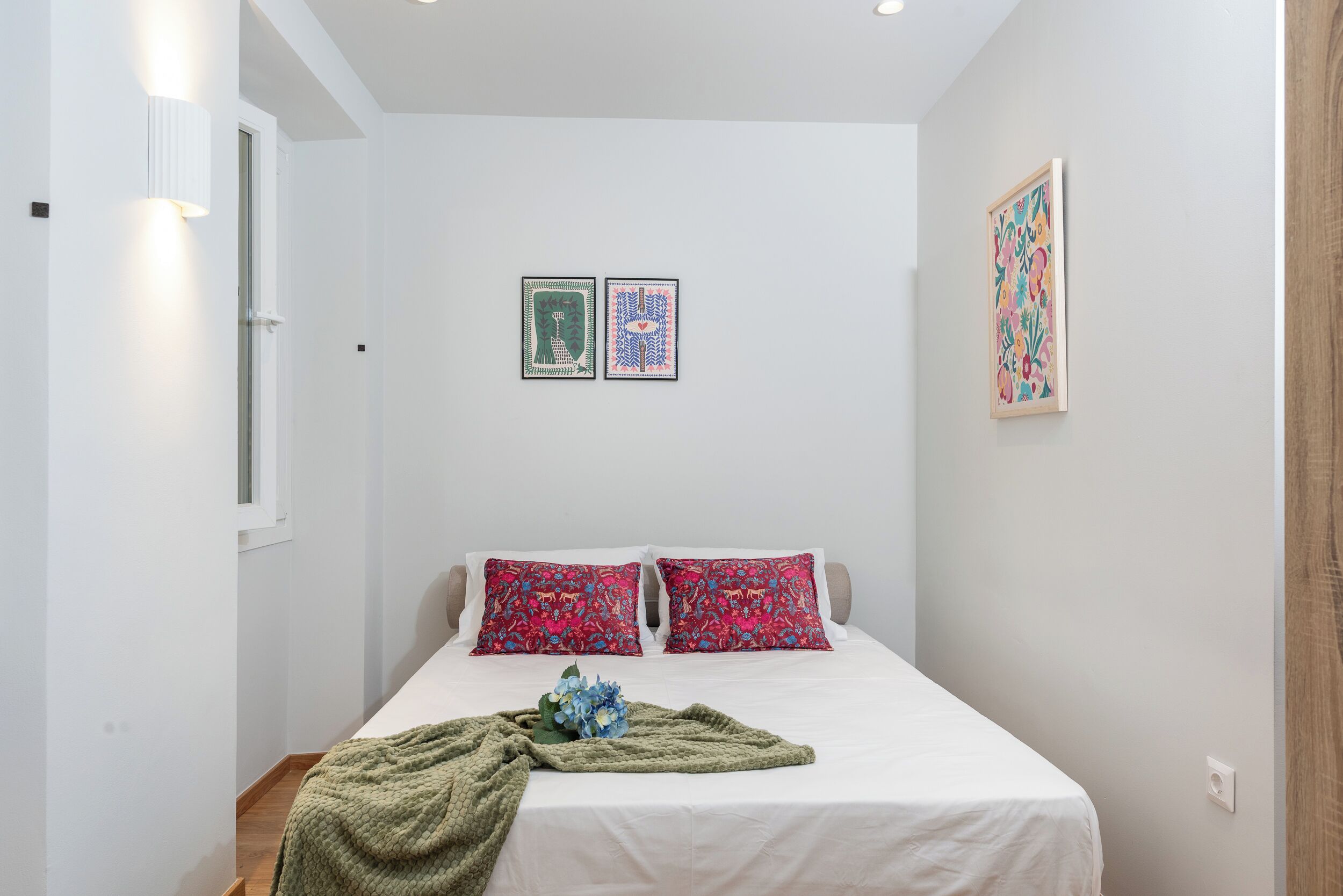 A bedroom with a bed, two pillows, a blanket, and two wall-mounted artworks.