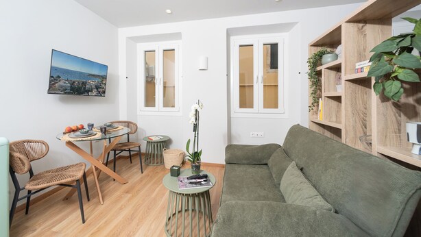 Un salon moderne avec une table à manger à plateau de verre, des chaises en osier, un canapé vert et une bibliothèque en bois.