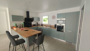 A modern kitchen with a central island, two bar stools, a built-in oven, and a window providing natural light. - La maison du Soleil 4* ☀️,completed in 2025,near RN12 with high-speed wifi (Bodilis)