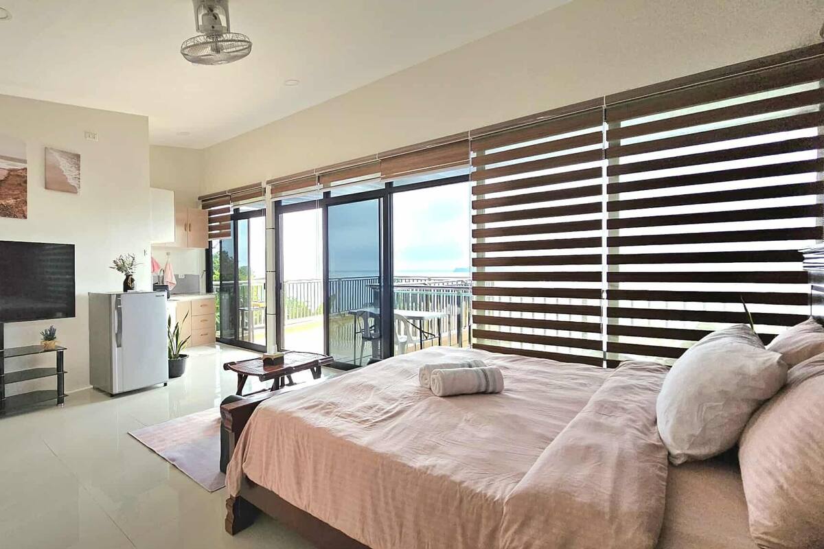 Une chambre moderne dotée d’un grand lit, d’un téléviseur à écran plat, d’une table à manger et d’un balcon avec vue.