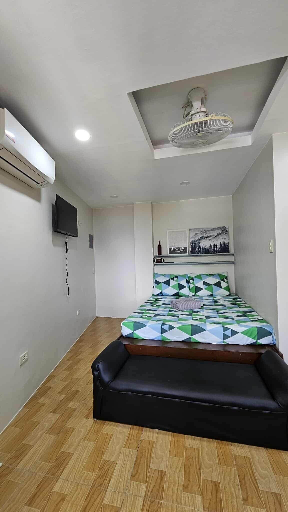 A bedroom with a bed, a ceiling fan, an air conditioner, and a mounted TV.