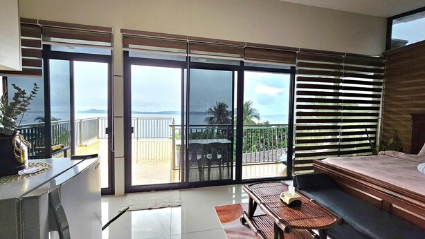 Ein Balkon mit Blick auf das Meer, ein Bett, ein Schreibtisch und ein Stuhl.