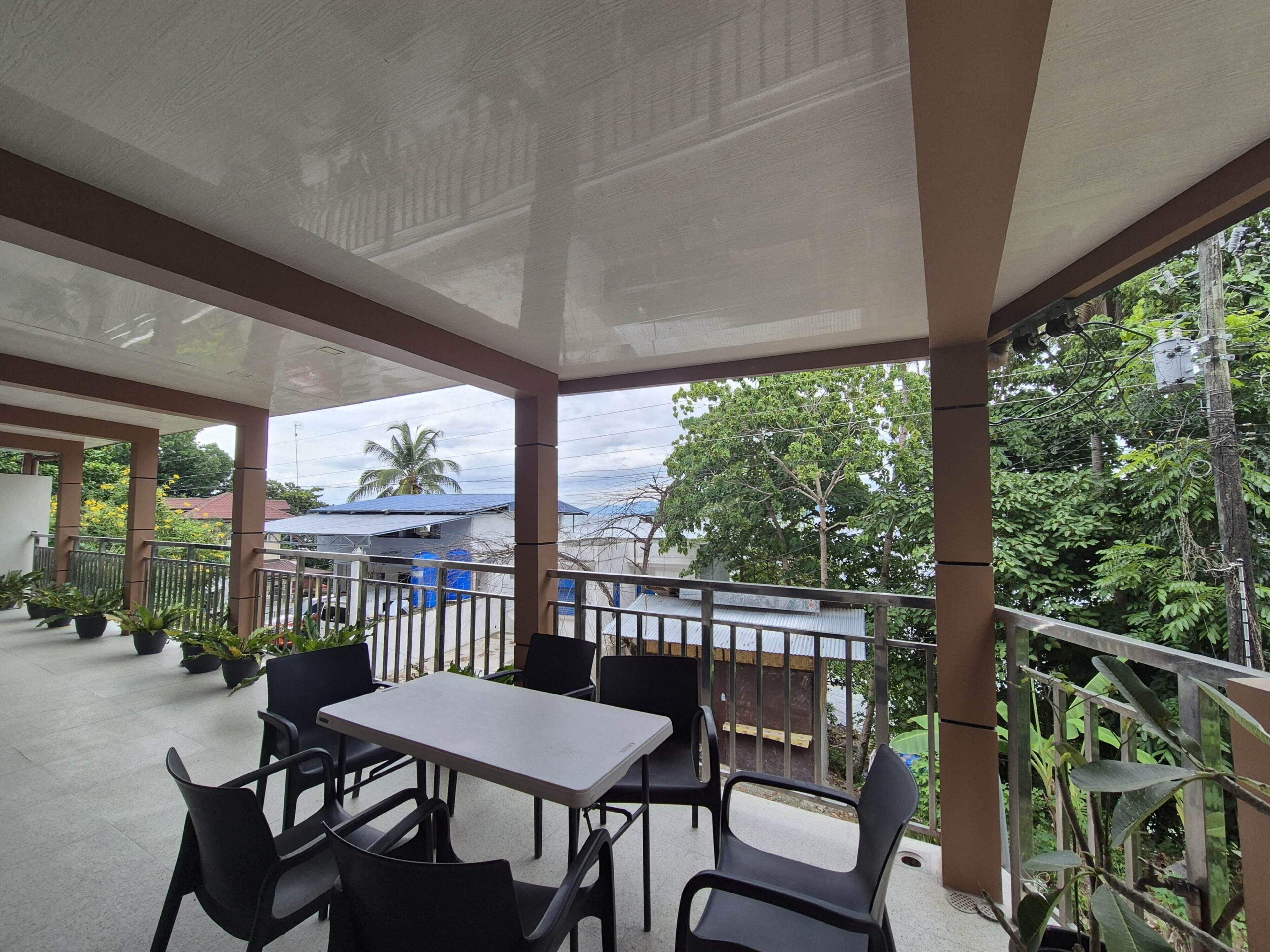 A covered outdoor seating area with tables and chairs, overlooking a residential area with trees and houses.
