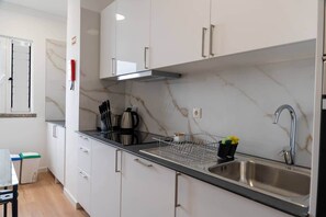 A modern kitchen with white cabinets, a stainless steel sink, and a black countertop. - Ocean View Balcony Apartment in Garajau, Madeira  Perfect R (Caniço)