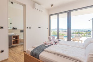 Quarto de hotel moderno com uma cama grande, banheiro com pia e espelho, e varanda com vista para a cidade.